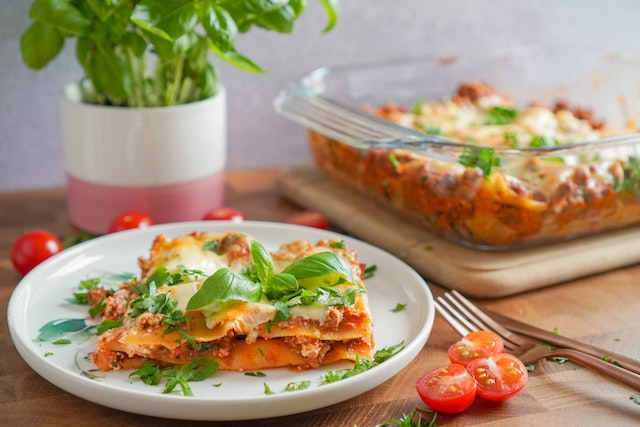 Lasagna in a glass dish with a serving on a plate in the foreground